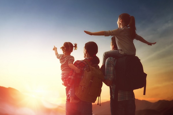 Mother, father and two children looking at a sunrise in the mountains.  Father carrying one of the children on his back