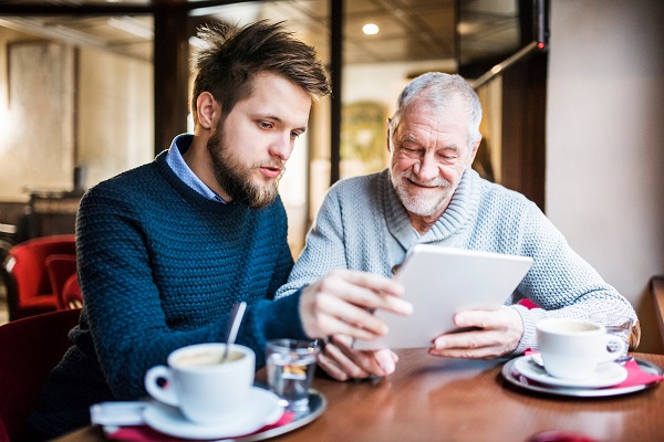 2 men sat at a table with coffees using a tablet device